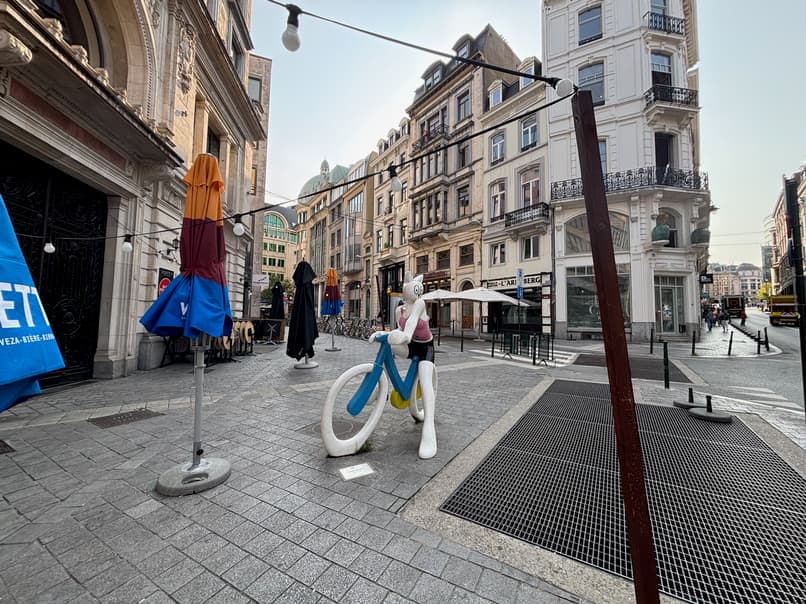 An outdoor street scene with a large, whimsical statue of a cartoon cat riding a bicycle in the foreground.